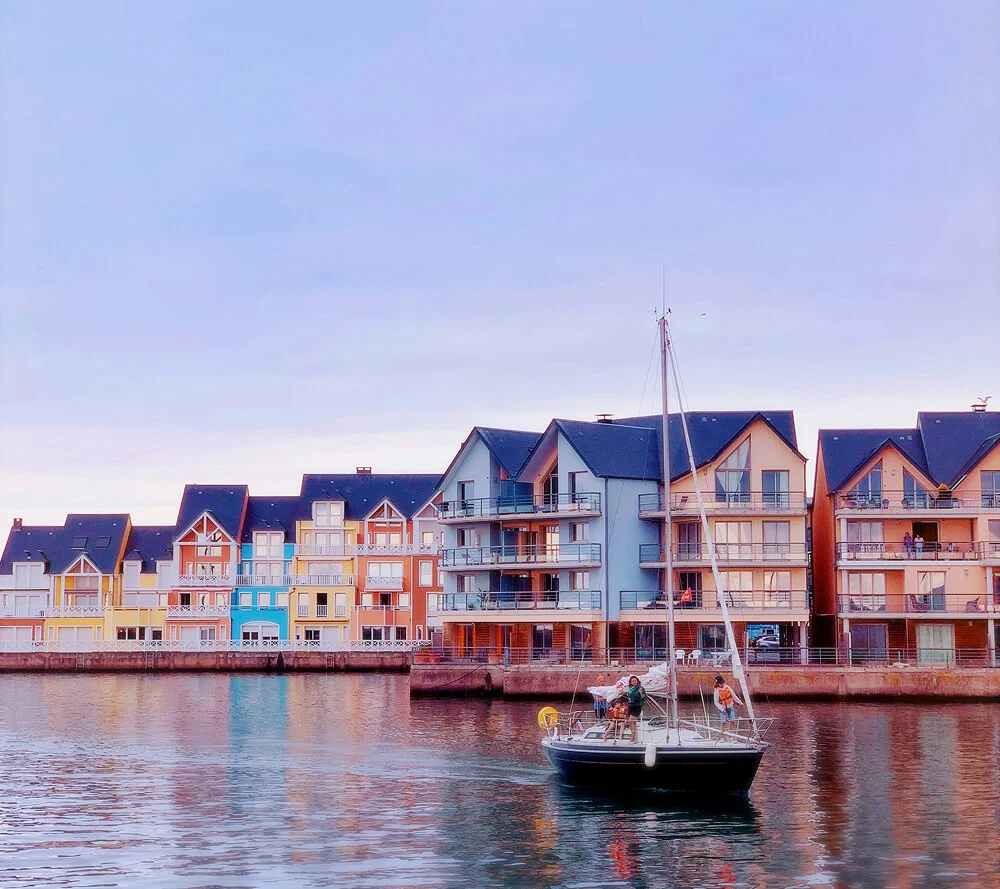 Bateau à voile sur le port de Deauville avec en arrière-plan les façades colorées des bâtiments normands.
