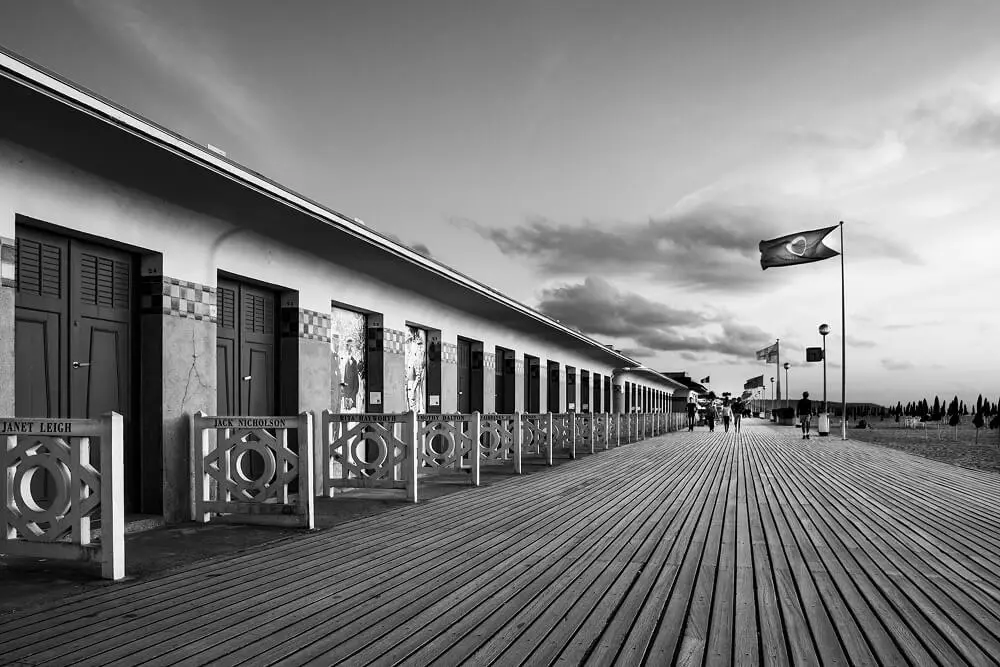 Planches des célèbres Planches de Deauville avec ses cabines et son drapeau, en noir et blanc.