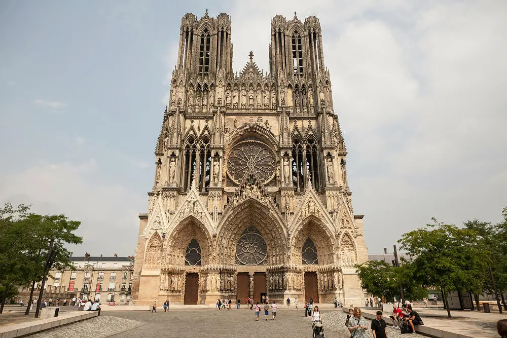 Façade de la Cathédrale Notre-Dame de Reims en France, avec ses tours gothiques et ses détails sculptés, sous un ciel bleu.