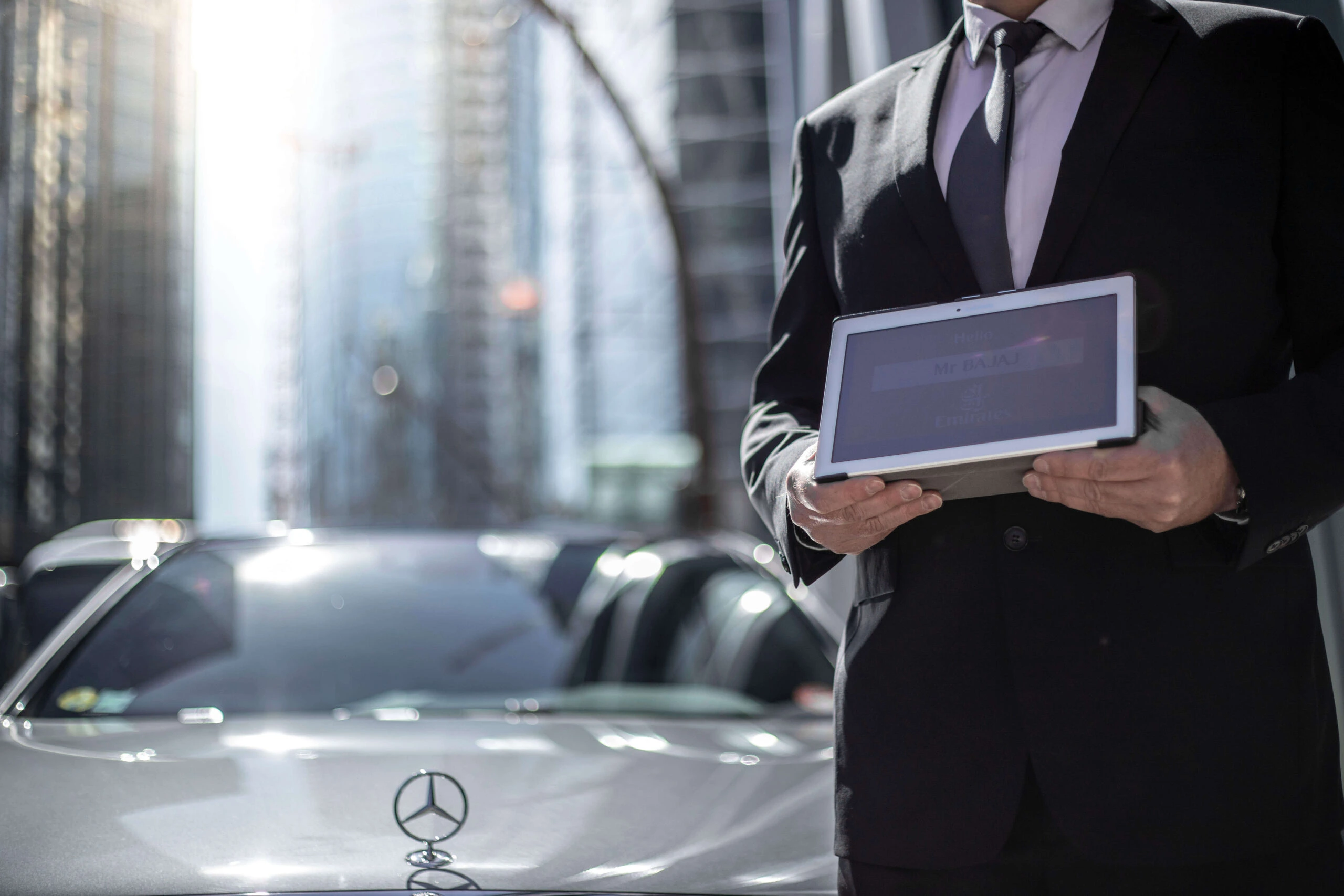 Chauffeur Service Prestige en costume tenant une tablette de bienvenue, illustrant le service Meet & Greet et l'accueil personnalisé.