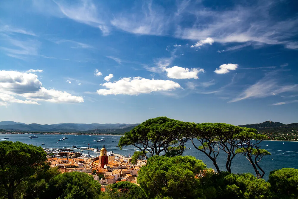 Vue aérienne de Saint-Tropez en été, avec son clocher iconique, le port et la mer Méditerranée sous un ciel bleu.