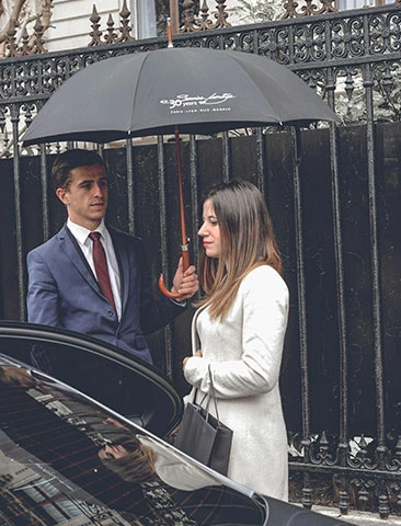 Chauffeur Service Prestige tenant un parapluie pour une cliente, offrant un service de mise à disposition.
