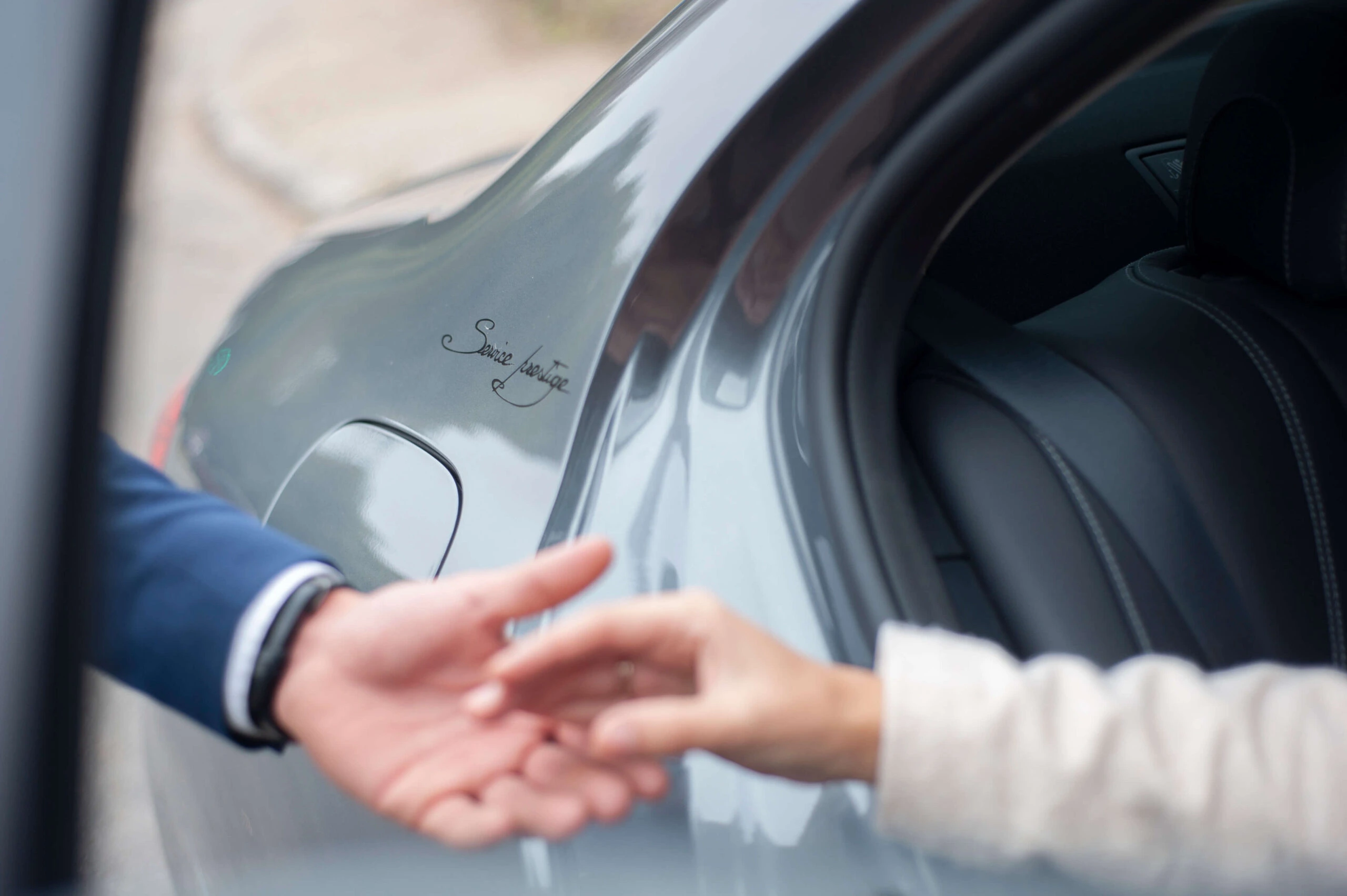Main d'un chauffeur Service Prestige tendant la main pour aider un passager à monter dans une voiture de luxe, symbolisant le service personnalisé et l'assistance.